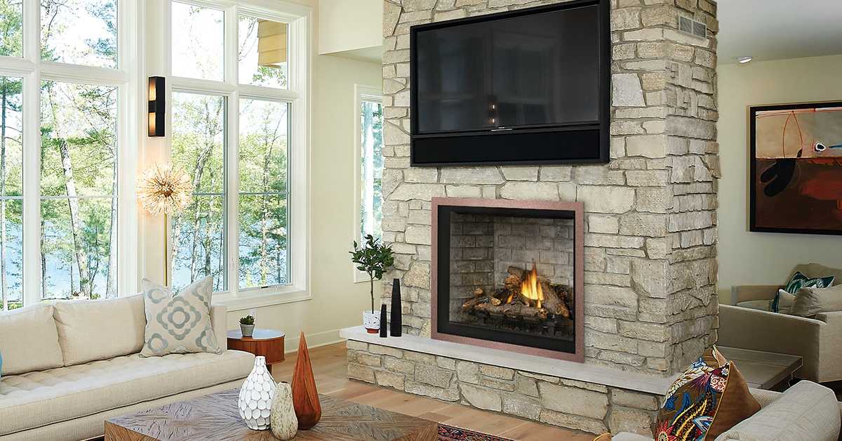 Napoleon gas fireplace built into a floor-to-ceiling stone chimney with a wall-mounted TV above in a bright lakefront living room